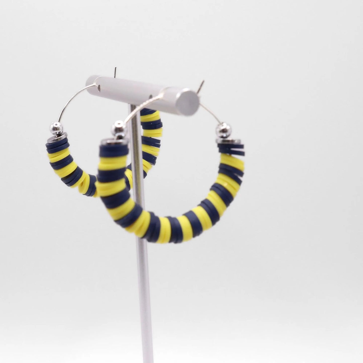 Navy blue and yellow heishi bead hoop earrings with silver accents displayed on a branded card against a clean white background