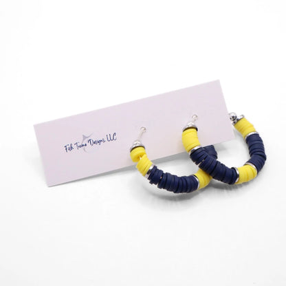 Navy blue and yellow heishi bead hoop earrings with silver accents hanging on a minimalist jewelry stand against a white background
