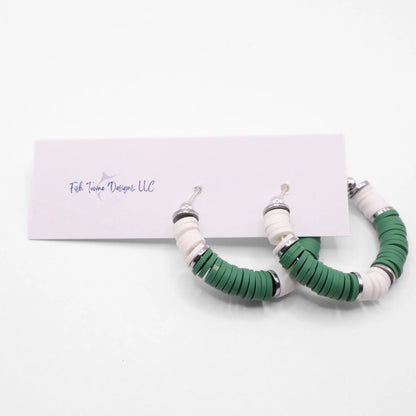 Green and white heishi bead hoop earrings with silver accents hanging on a minimalist jewelry stand against a white background