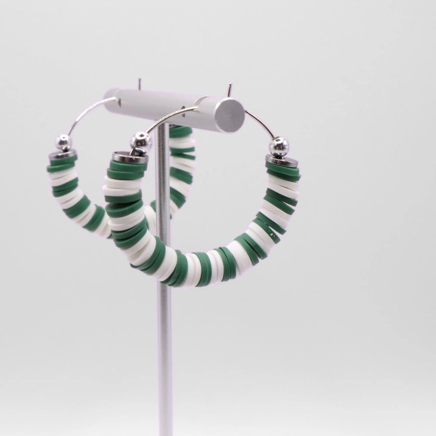 Close-up of green and white heishi bead hoop earrings with silver accents on a jewelry stand, highlighting bead detail and pattern