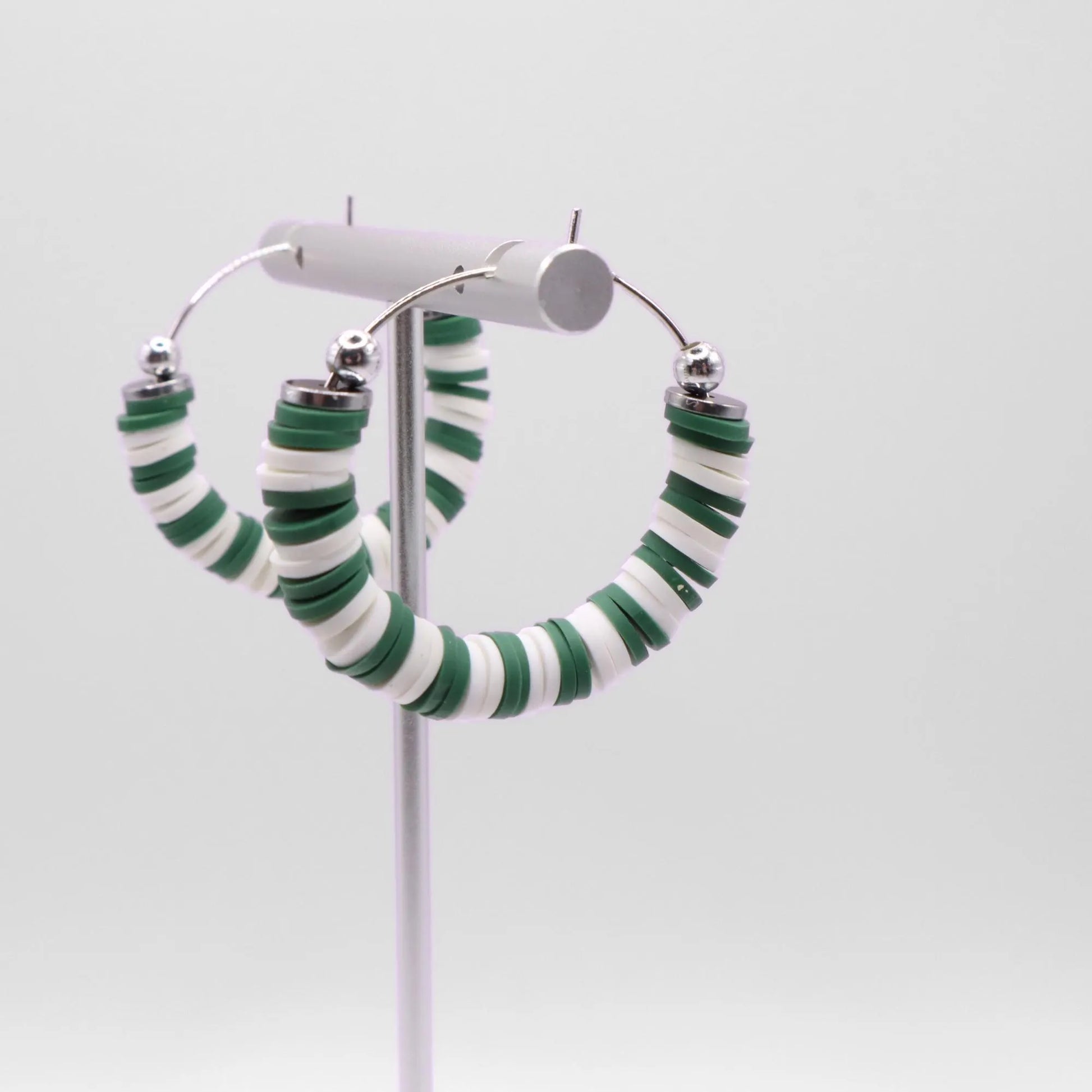 Close-up of green and white heishi bead hoop earrings with silver accents on a jewelry stand, highlighting bead detail and pattern