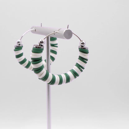 Close-up of green and white heishi bead hoop earrings with silver accents on a jewelry stand, highlighting bead detail and pattern