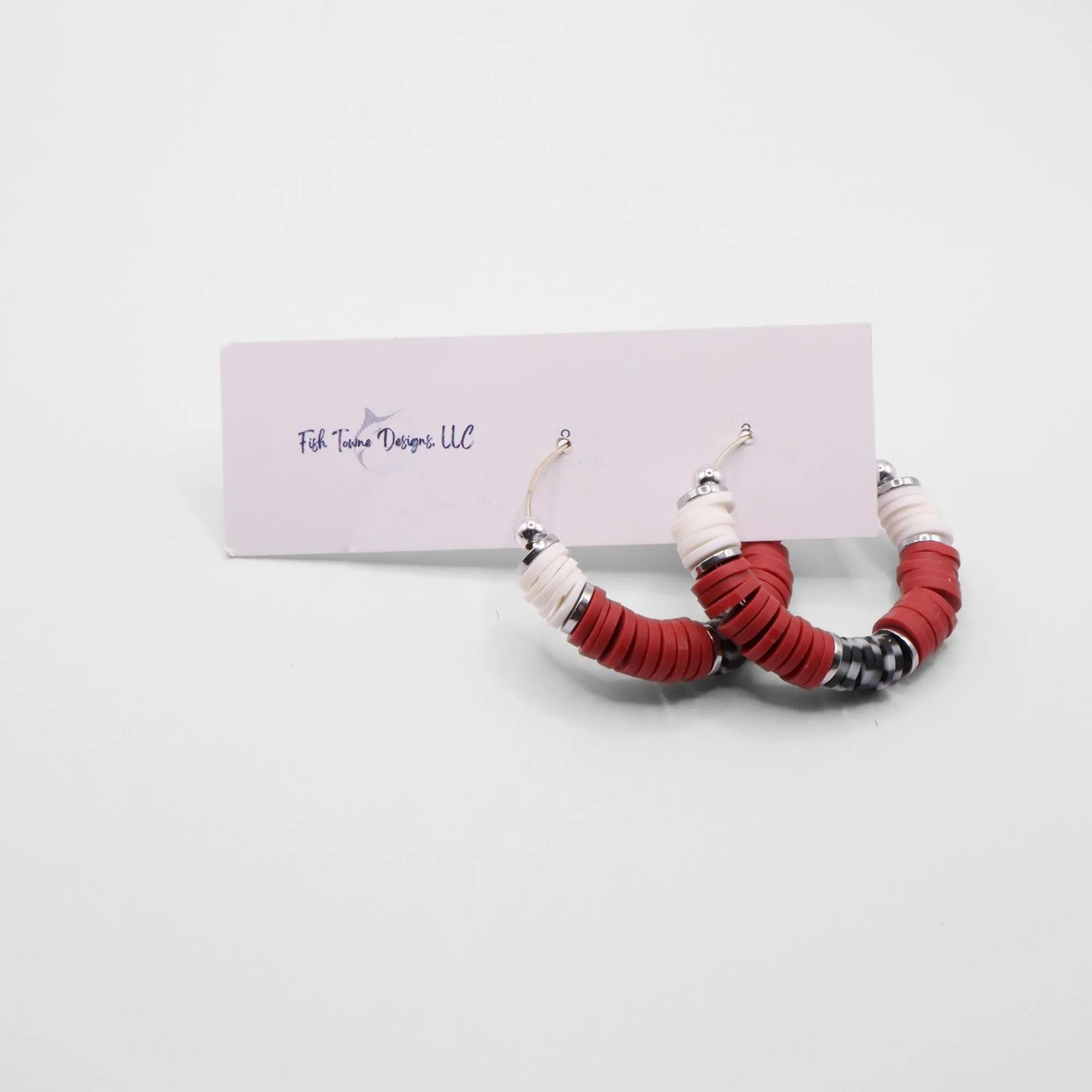 Crimson and houndstooth heishi bead hoop earrings with silver accents hanging on a minimalist jewelry stand against a white background
