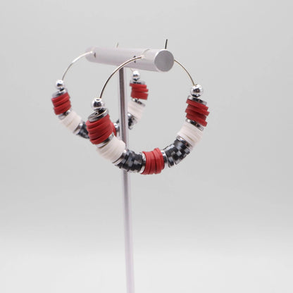 Side angle view of crimson and houndstooth heishi bead hoop earrings with silver spacers on a display stand against a white background