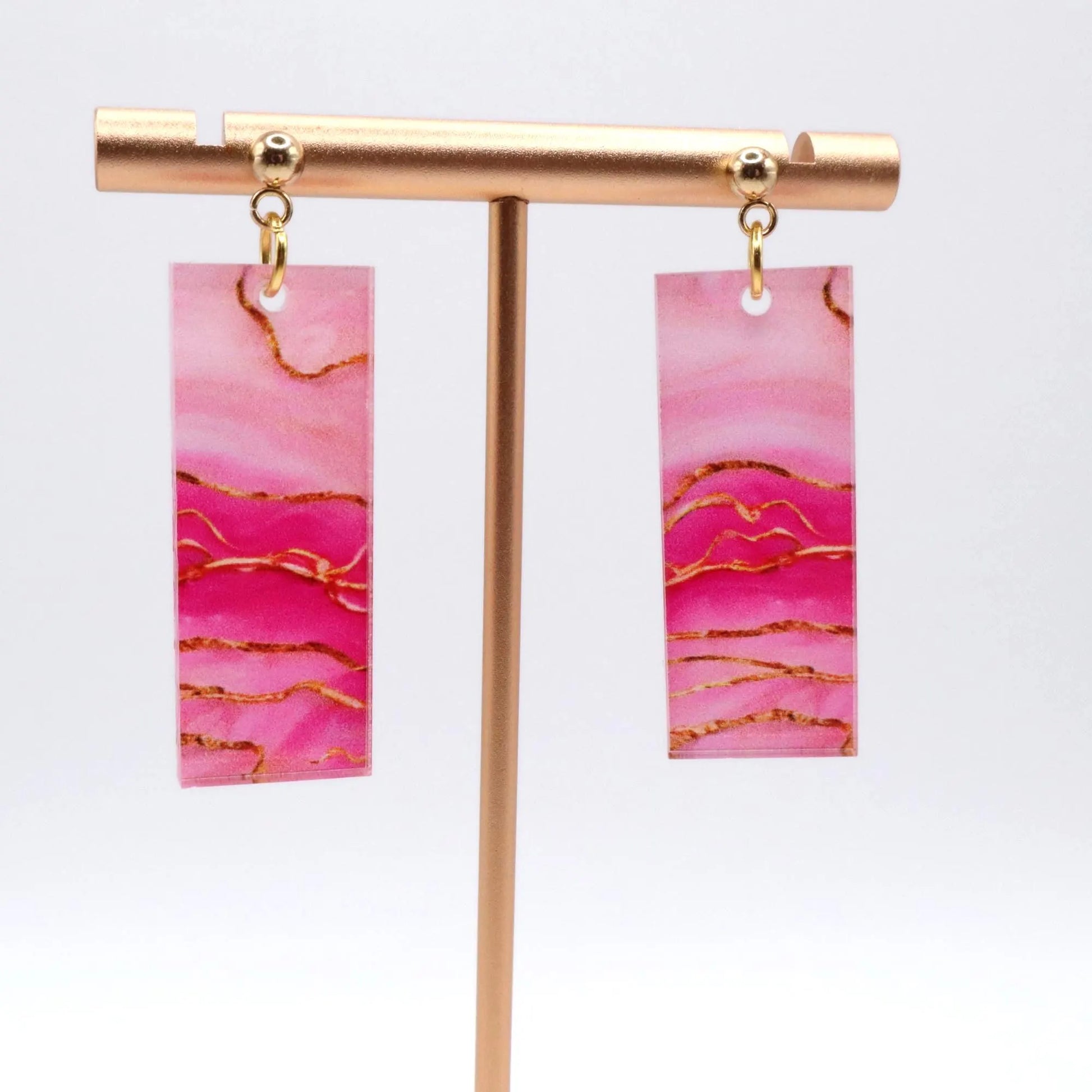 Pink marbled earrings with gold accents on a gold earring stand against a white background