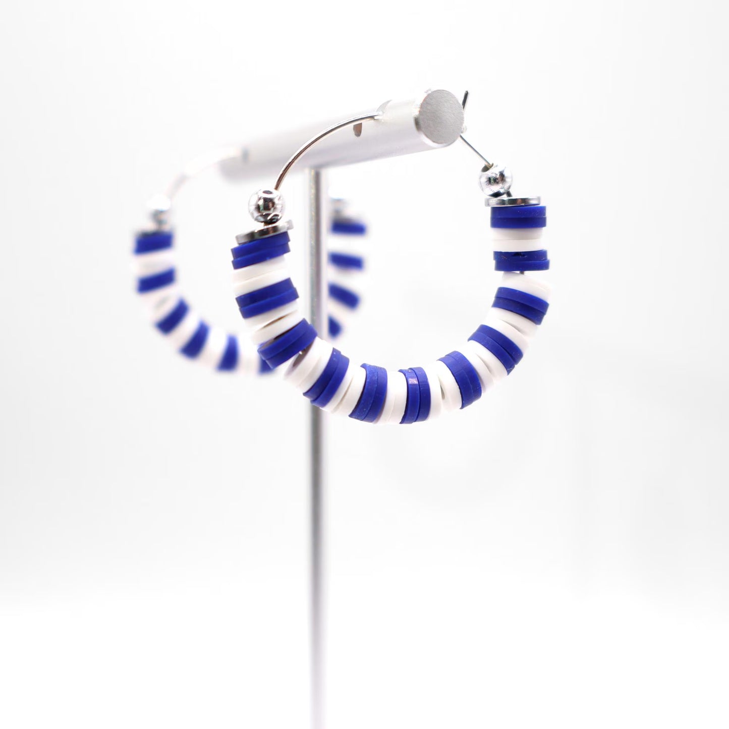 Close-up of royal blue and white heishi bead hoop earrings with silver accents on a jewelry stand, highlighting bead detail and pattern