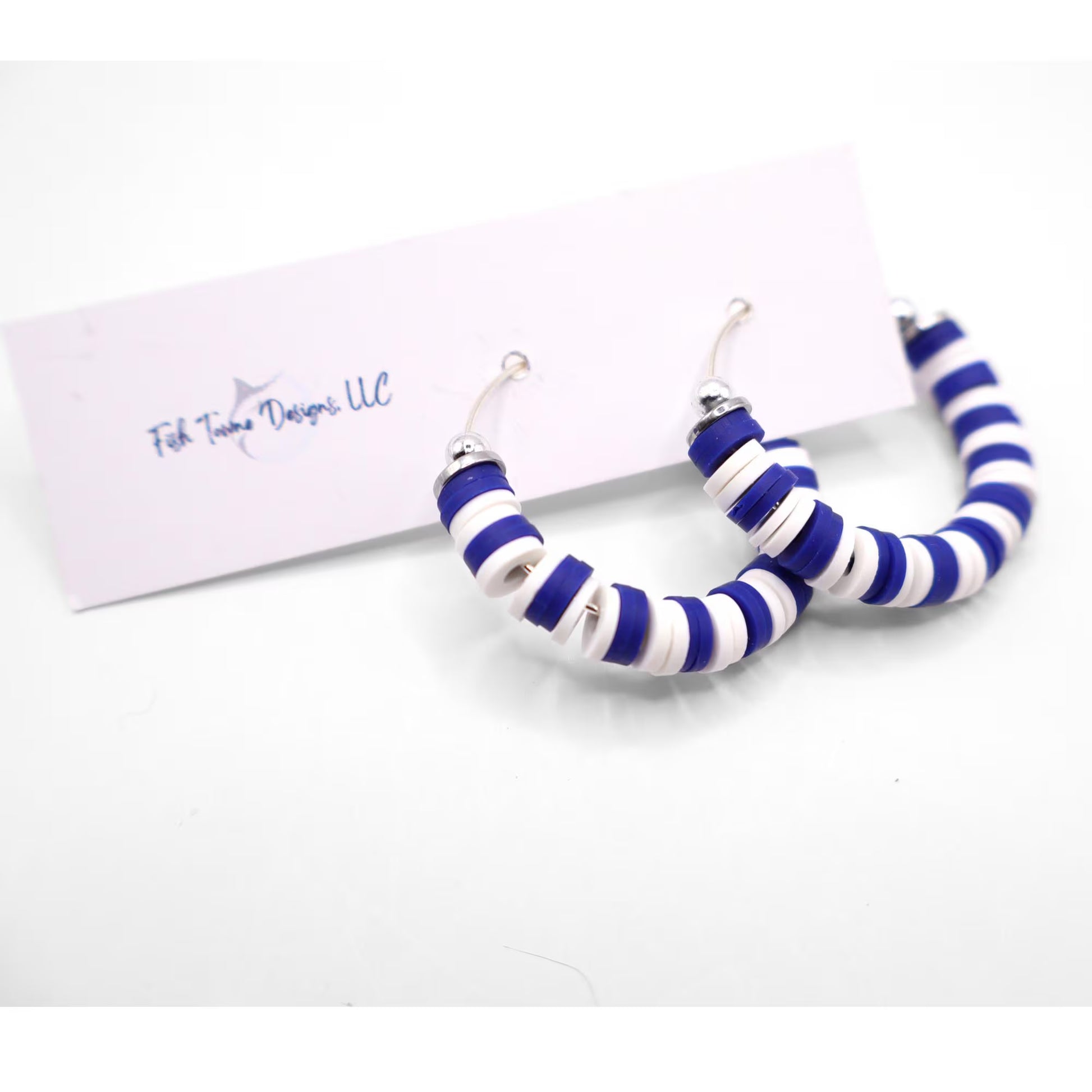 Royal blue and white heishi bead hoop earrings with silver accents displayed on a branded card against a white background