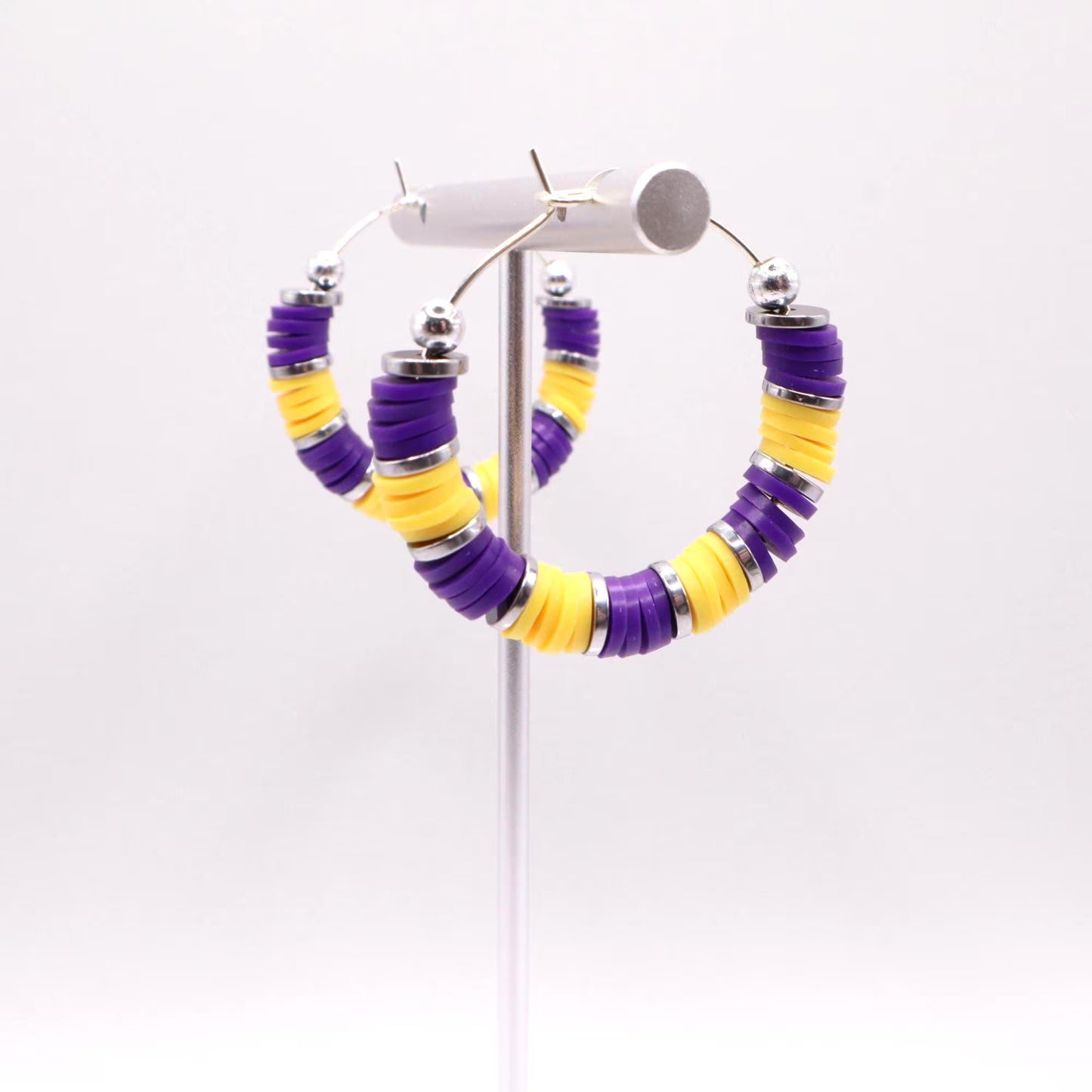 Side angle view of purple and gold heishi bead hoop earrings with gold spacers on a display stand against a white background