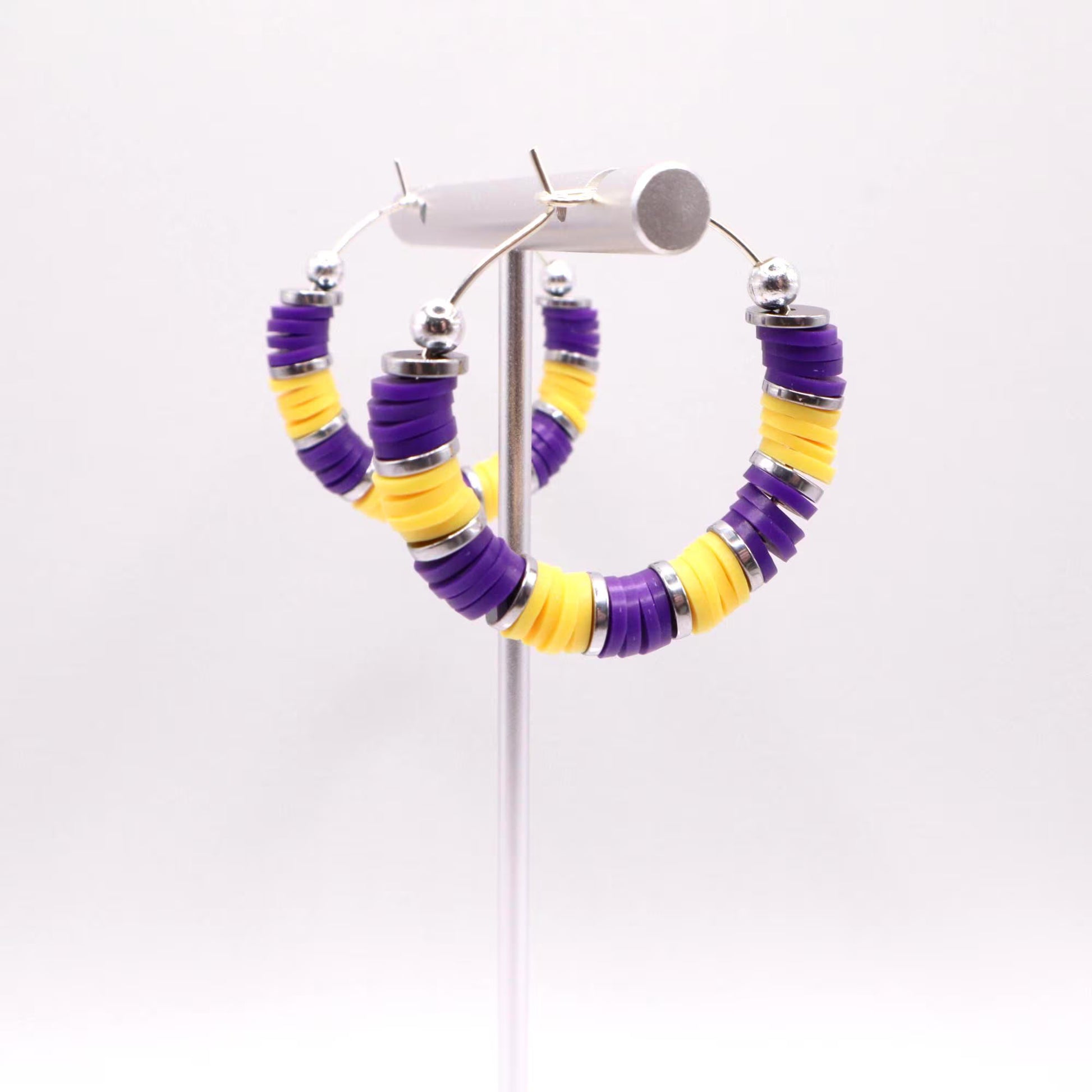 Side angle view of purple and gold heishi bead hoop earrings with gold spacers on a display stand against a white background