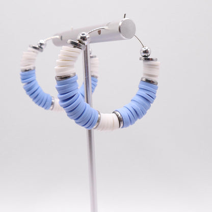 Side angle view of light blue and white heishi bead hoop earrings with silver spacers on a display stand against a white background