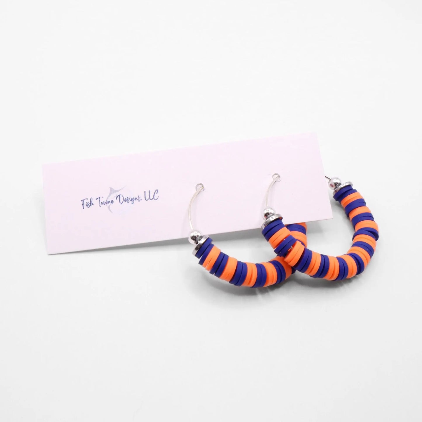 Blue and orange heishi bead hoop earrings with silver accents displayed on a branded card against a white background