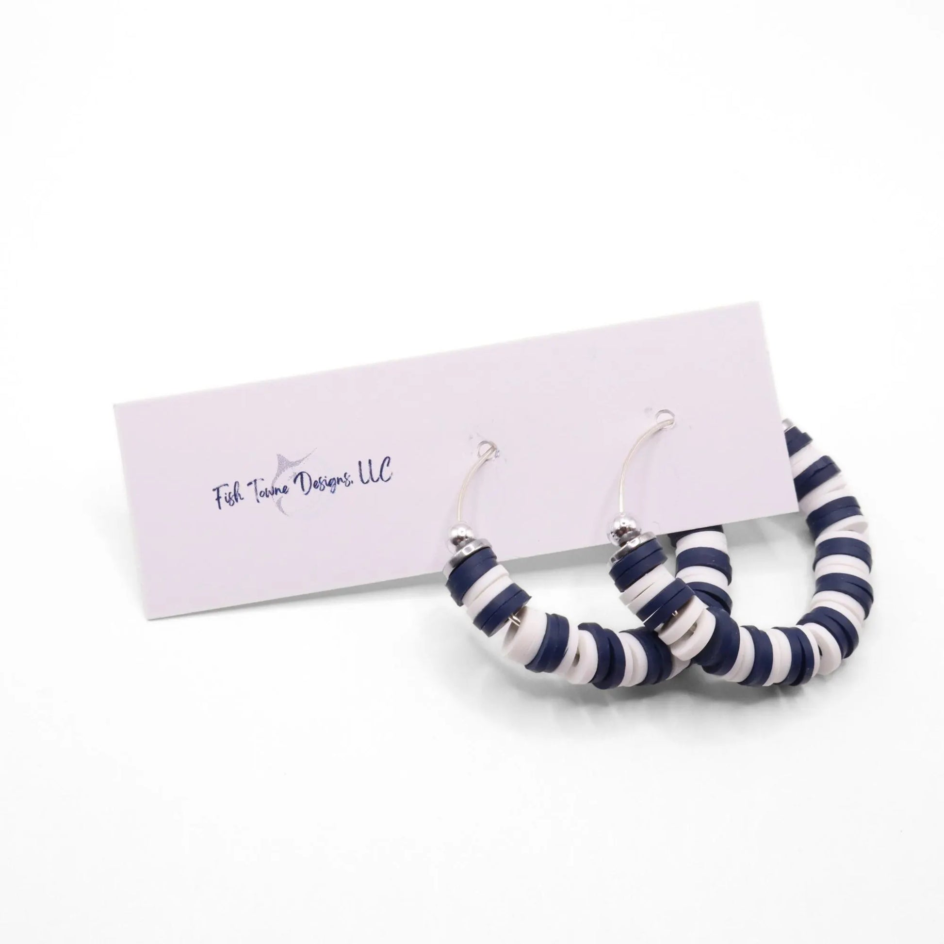 Navy blue and white heishi bead hoop earrings with silver accents displayed on a branded card against a white background