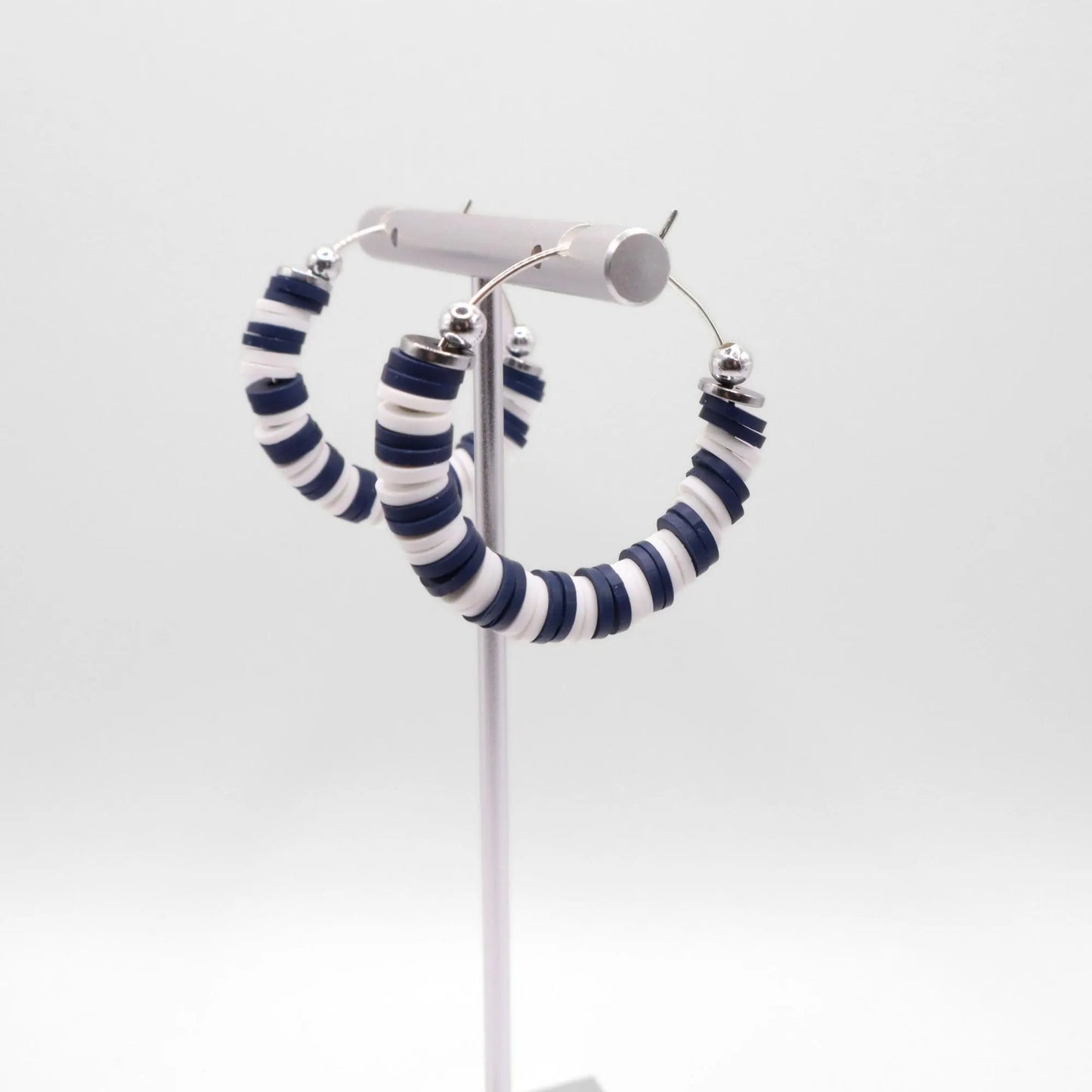 Navy blue and white heishi bead hoop earrings with silver accents displayed on a branded card against a clean white background