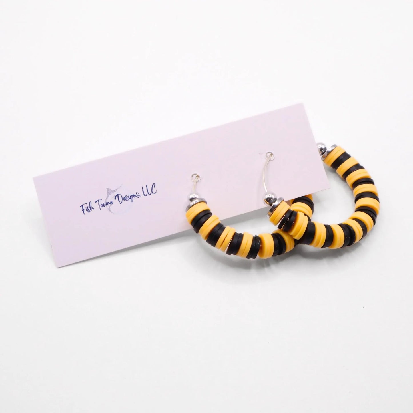 Black and yellow heishi bead hoop earrings with silver accents displayed on a branded card against a white background