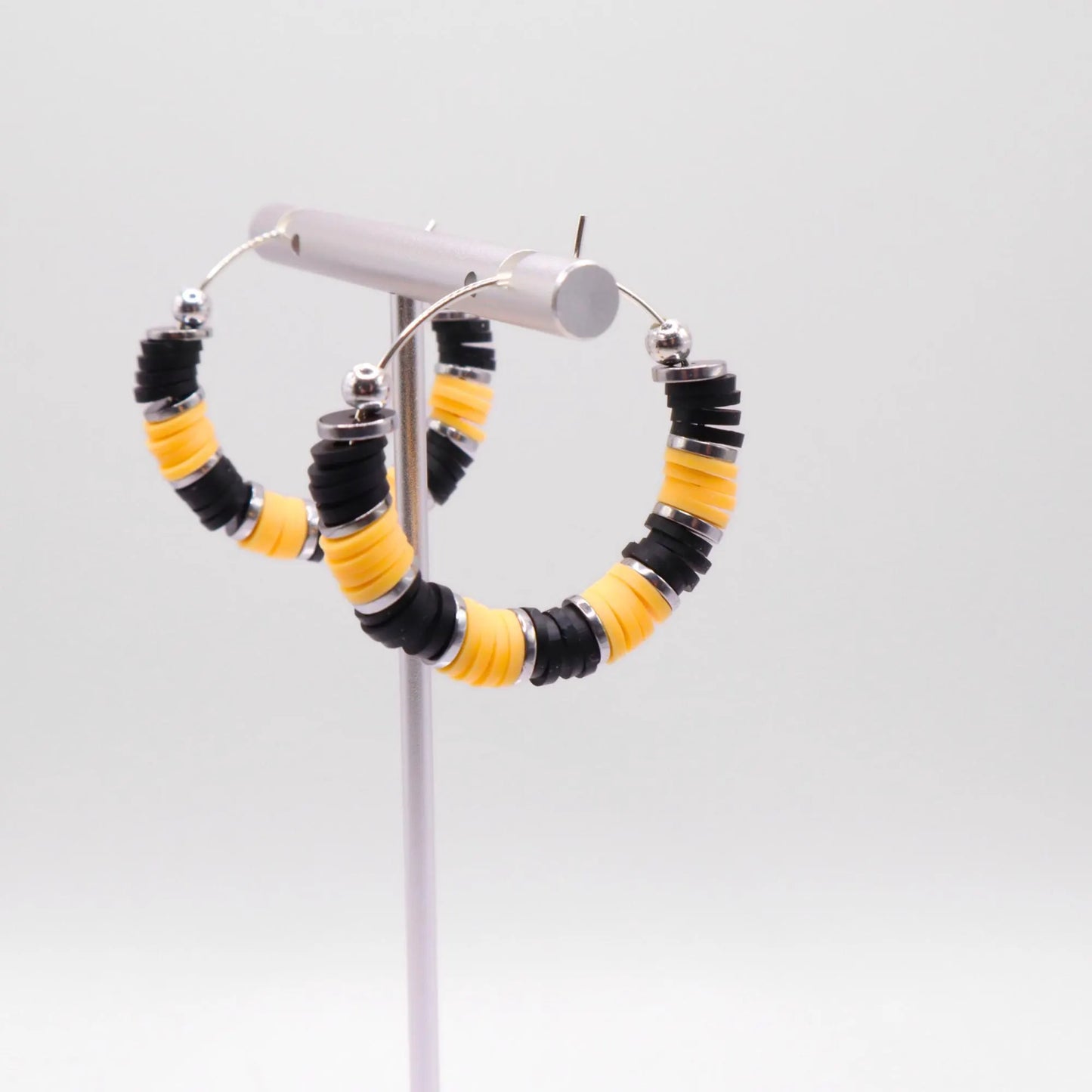 Black and yellow heishi bead hoop earrings with silver accents displayed on a branded card against a clean white background