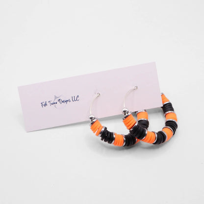 Side angle view of orange and black heishi bead hoop earrings with silver spacers on a display stand against a white background