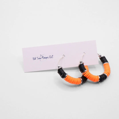 Orange and black heishi bead hoop earrings with silver accents displayed on a branded card against a clean white background