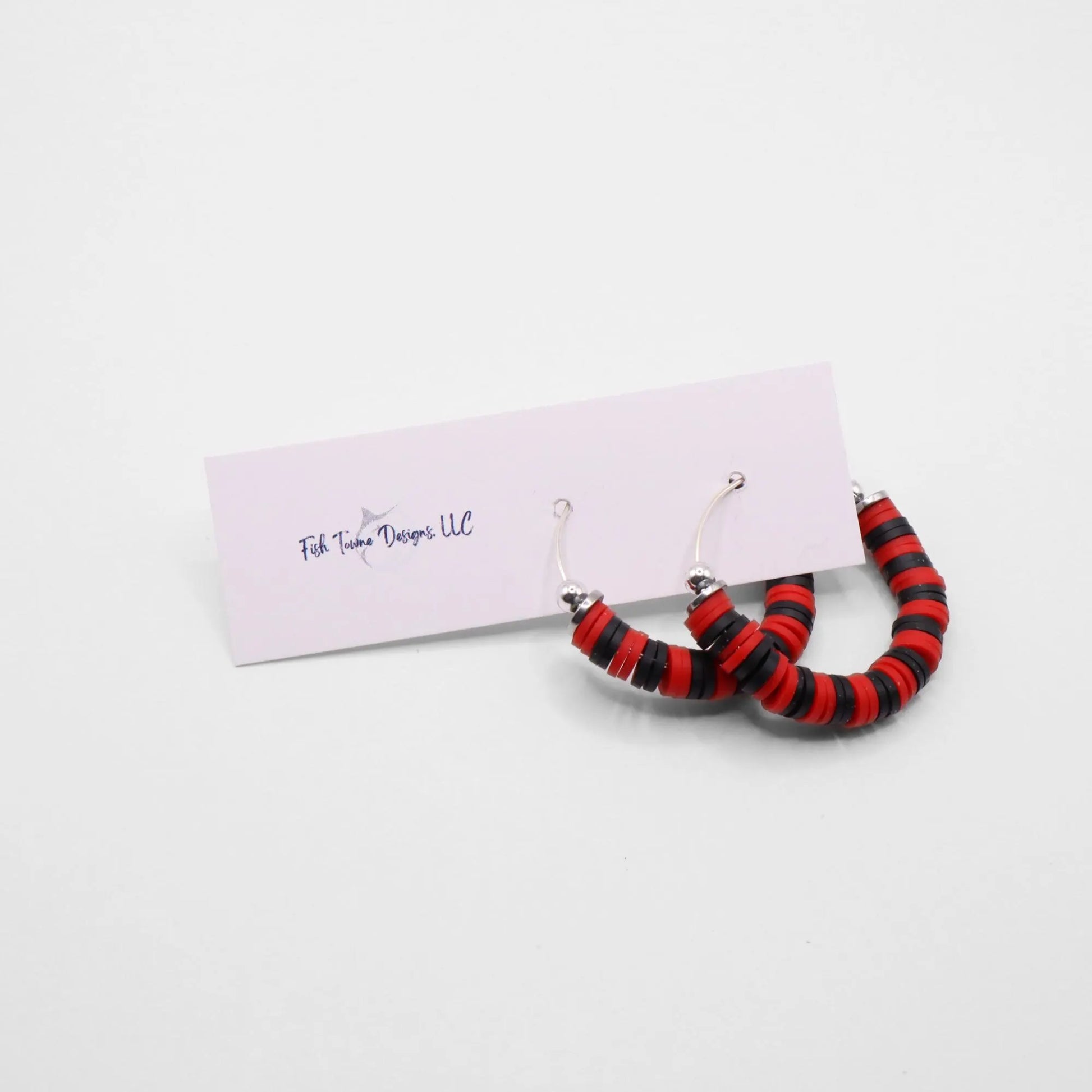 Close-up of red and black heishi bead hoop earrings with silver accents on a jewelry stand, highlighting bead detail and pattern