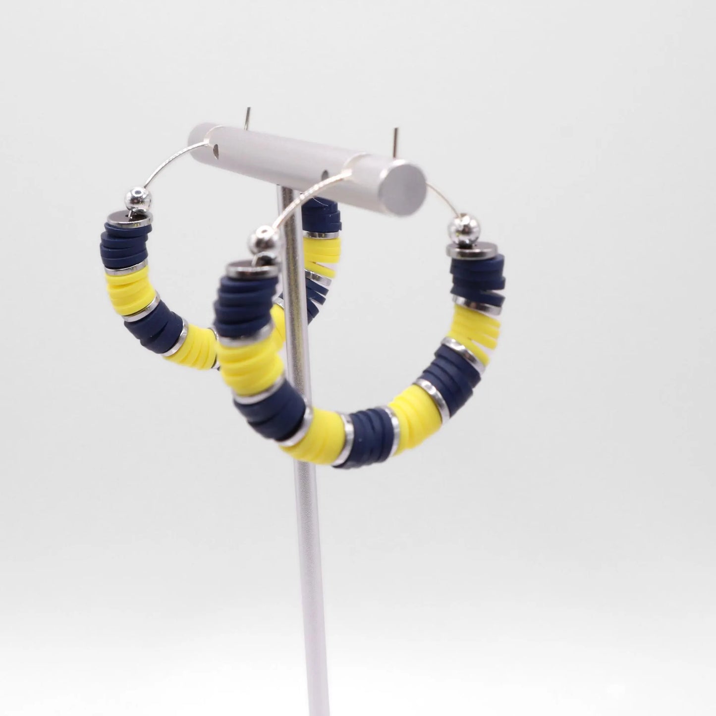 Side angle view of navy blue and yellow heishi bead hoop earrings with silver spacers on a display stand against a white background