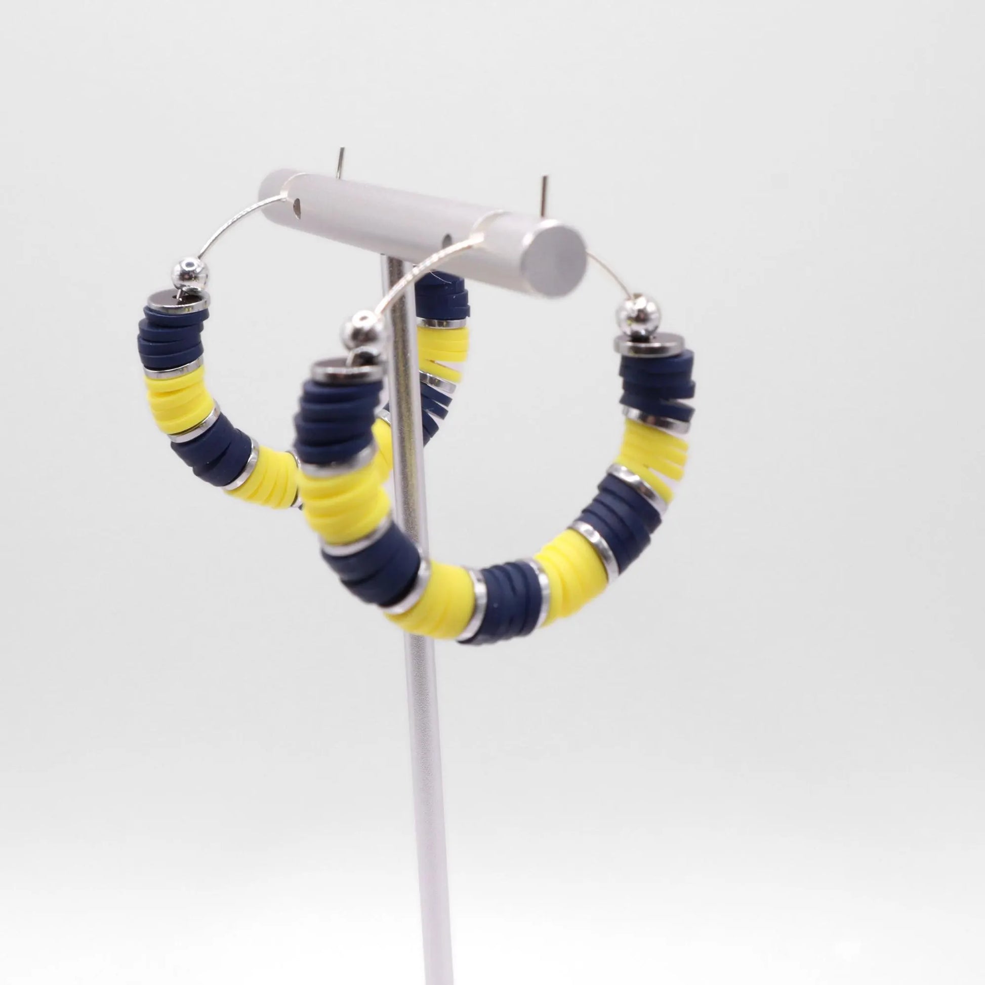 Side angle view of navy blue and yellow heishi bead hoop earrings with silver spacers on a display stand against a white background