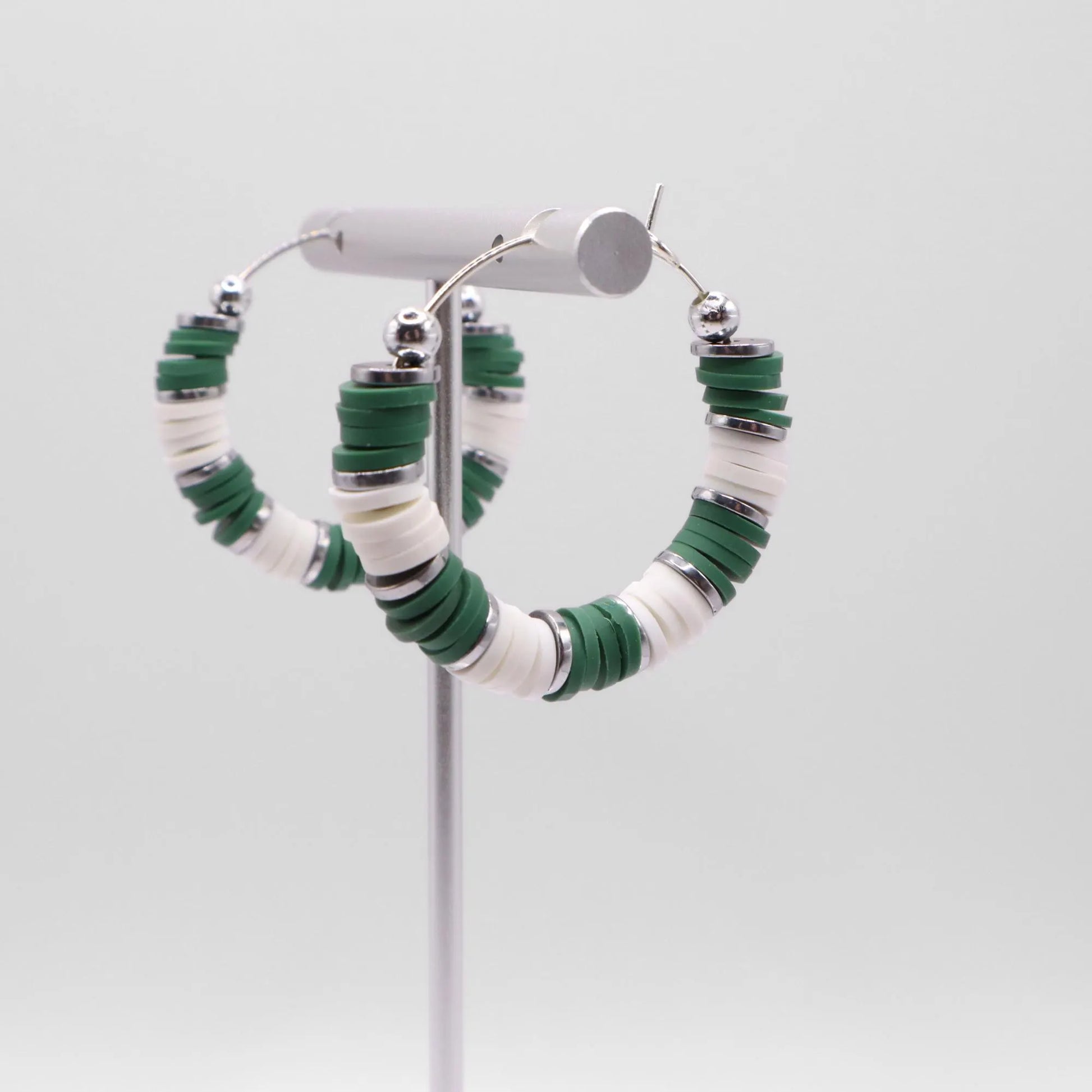 Side angle view of green and white heishi bead hoop earrings with silver spacers on a display stand against a white background