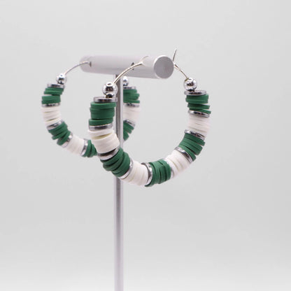 Side angle view of green and white heishi bead hoop earrings with silver spacers on a display stand against a white background