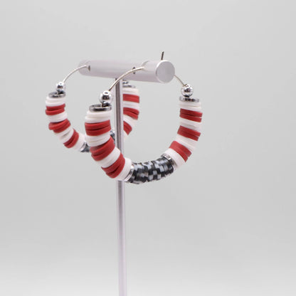 Close-up of crimson and houndstooth heishi bead hoop earrings with silver accents on a jewelry stand, highlighting bead detail and pattern