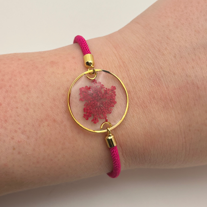 Bracelet with pink cord and gold clasp featuring a pink floral design on a wrist.
