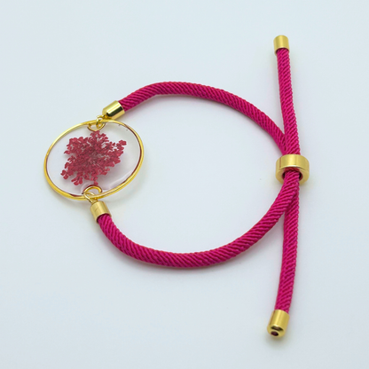 Flat lay of adjustable magenta cord bracelet with gold circle pendant and pressed floral design