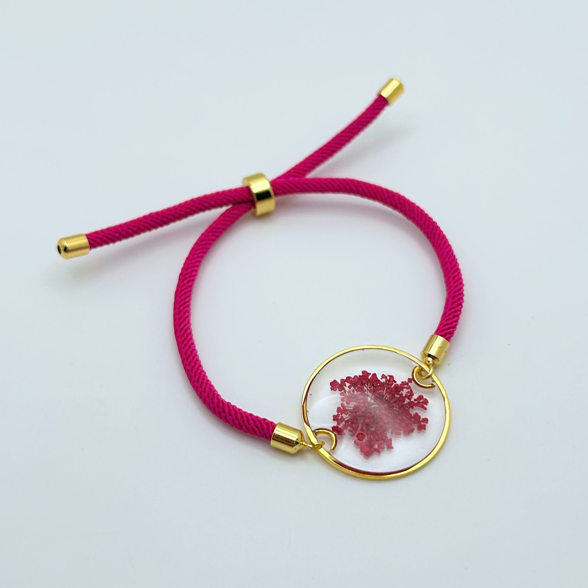 Pink bracelet with a gold clasp and prink floral charm on a light gray background