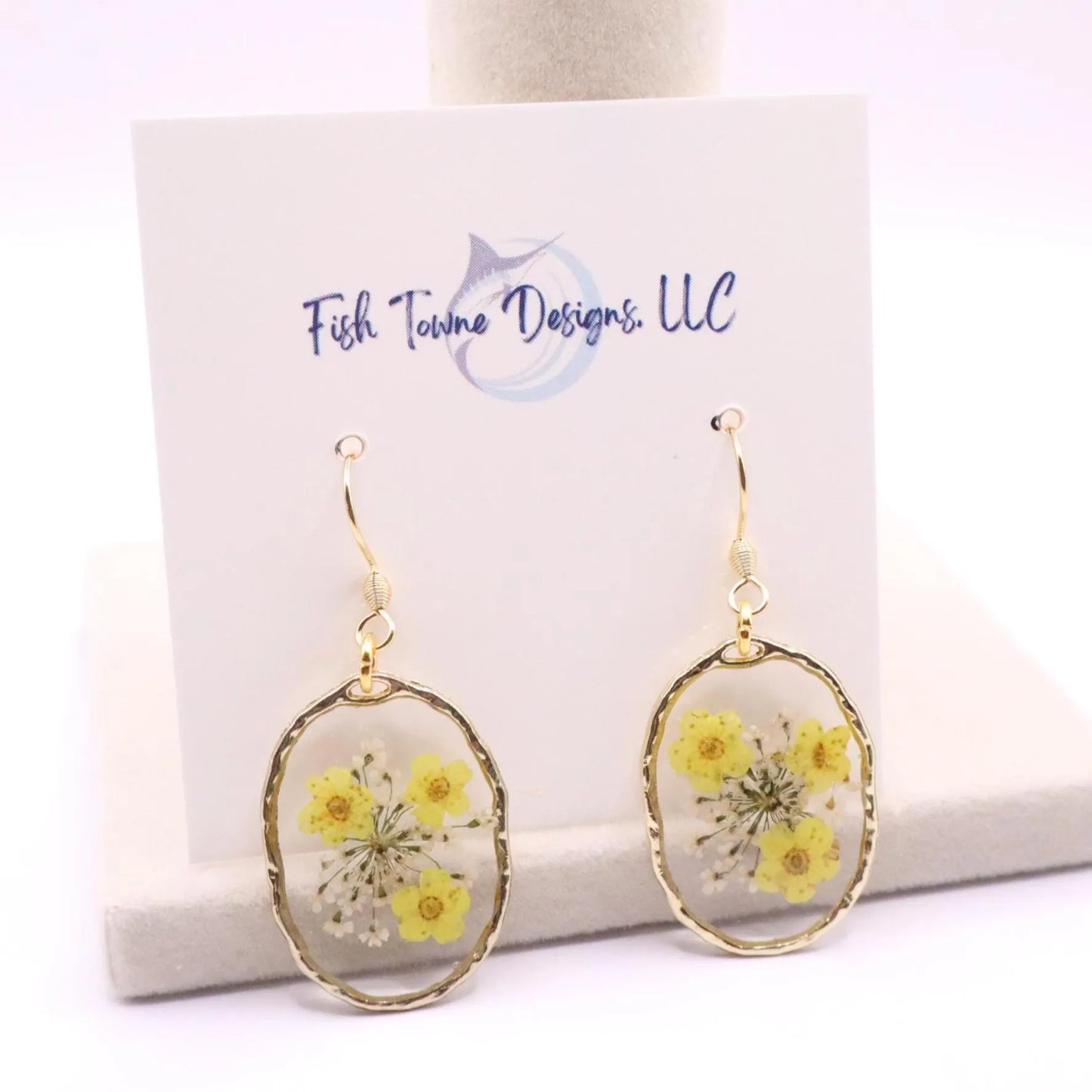 Clear resin earrings with real yellow pressed flowers and gold edge detail displayed on branded card with gold hook ear wires
