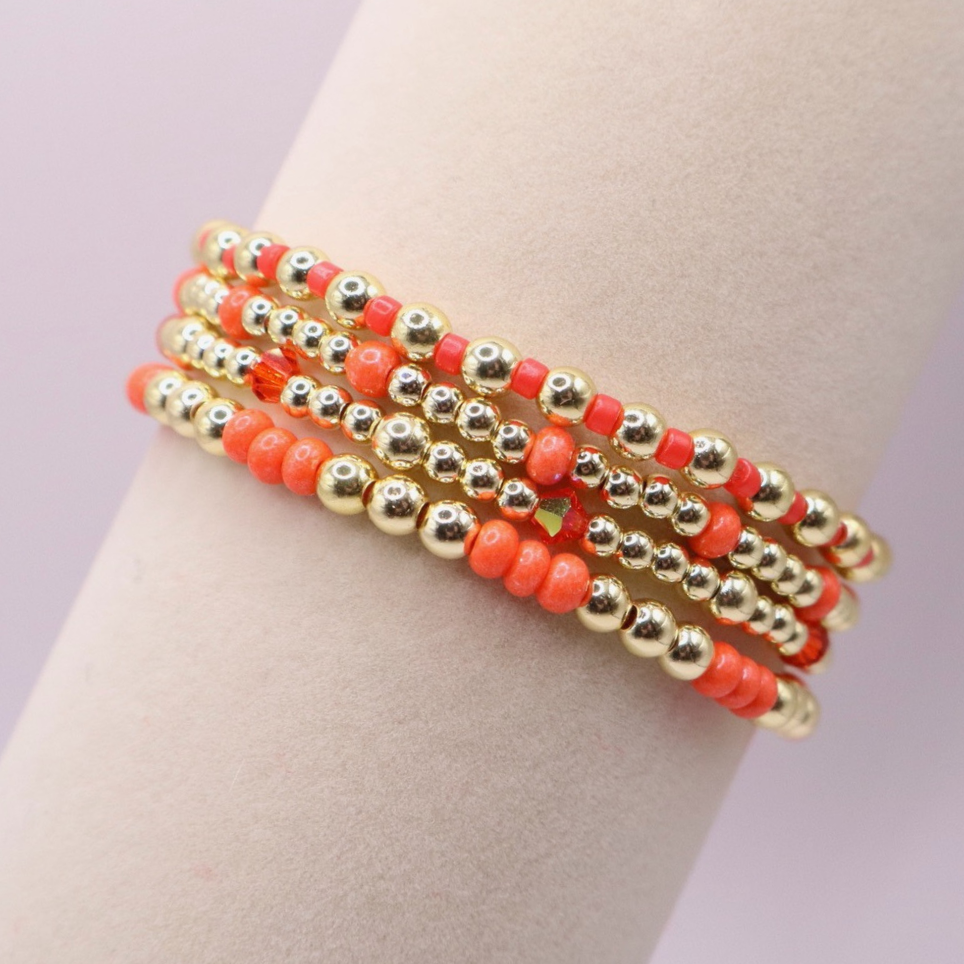Stack of handmade stretch bracelets featuring vibrant coral Preciosa seed beads, faceted crystal accents, and polished gold-tone hematite beads on a clean white background.