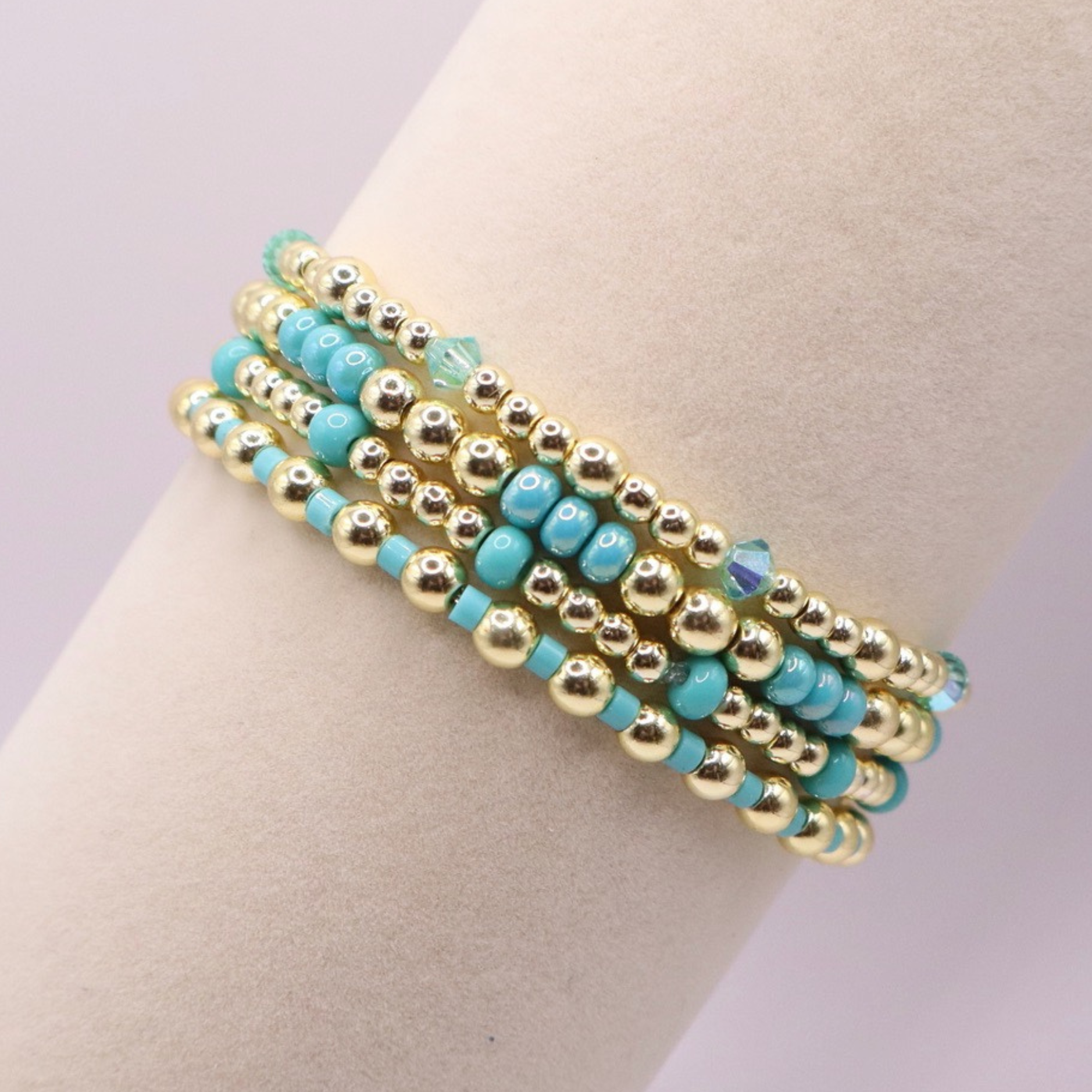 Layered bracelet stack with turquoise Preciosa seed beads, shimmering crystal accents, and gold-tone hematite beads on a clean white background.