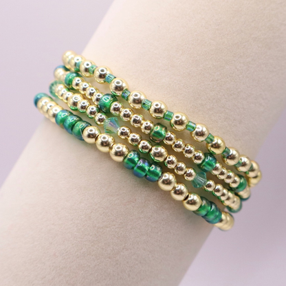 Handmade bracelet stack with green Preciosa seed beads, iridescent crystal accents, and polished gold-tone hematite beads on a clean white background.