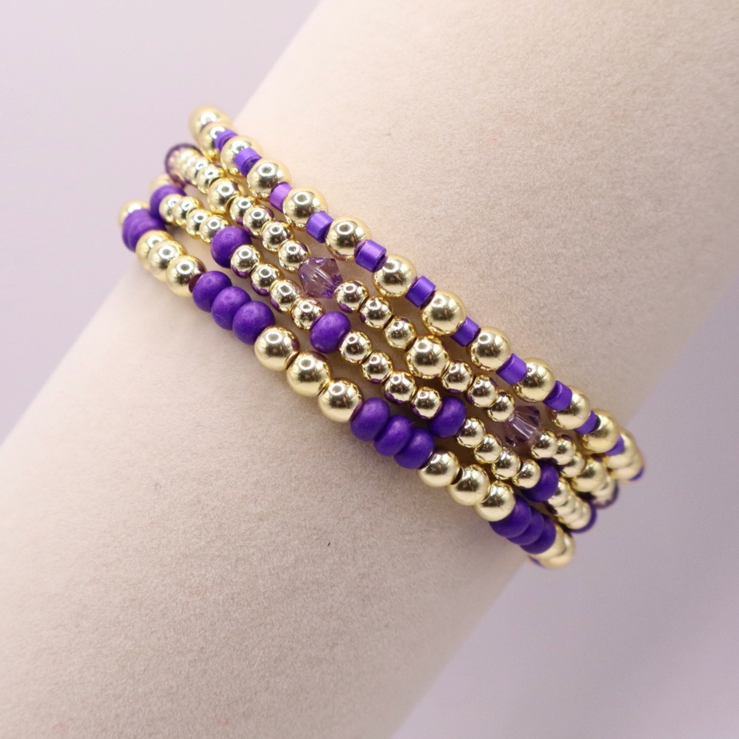 Elegant stack of stretch bracelets featuring rich purple Preciosa seed beads, faceted crystal details, and gold-tone hematite accent beads on a clean white background.