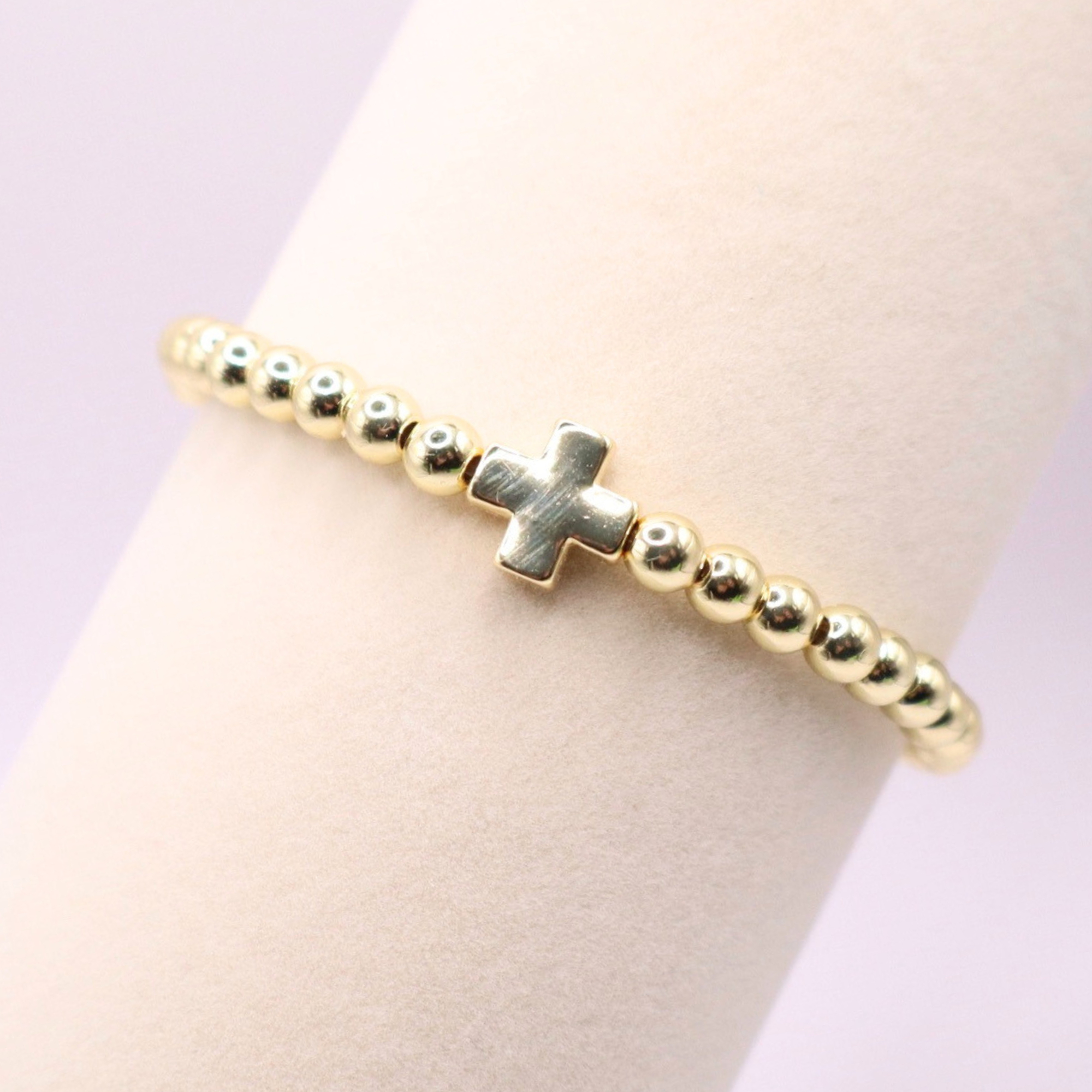 18K gold filled beaded stretch bracelet featuring a polished gold cross charm, styled on a wrist with a soft neutral background and minimalist luxe aesthetic.