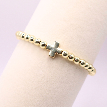 18K gold filled beaded stretch bracelet featuring a polished gold cross charm, styled on a wrist with a soft neutral background and minimalist luxe aesthetic.