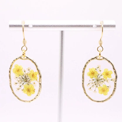 Lightweight floral resin dangle earrings with real yellow flowers suspended in clear resin and gold trimmed frame hanging on display stand