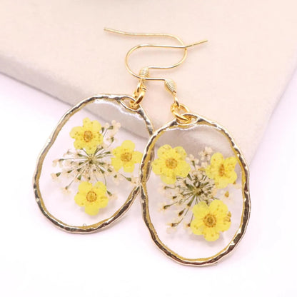 Real flower resin dangle earrings with yellow pressed flowers in clear resin framed in gold with gold hook ear wires on display